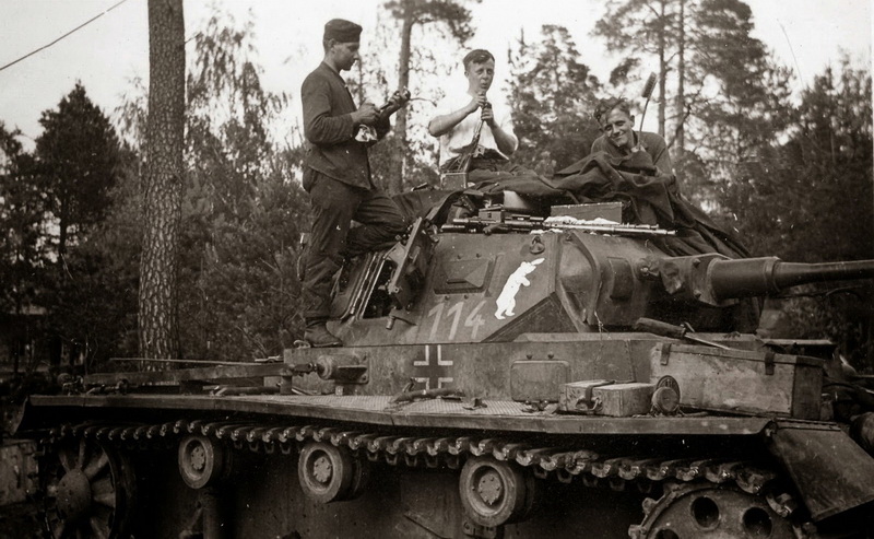 A Panzer III crew performs maintenance on their weapons including an MG 34 resting on the turret (Public Domain)